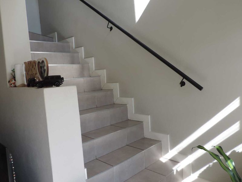 A bright staircase featuring neutral floor tiles and a modern black metal handrail, providing access between levels.
