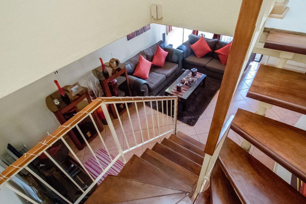 An elevated view looking down from a wooden staircase into a living room area with tiled flooring.