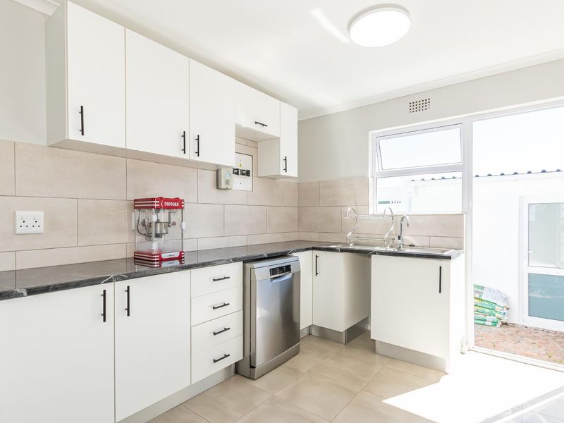 Modern kitchen featuring white cabinetry, stone-look countertops, tiled backsplash, and direct access to an outdoor area.