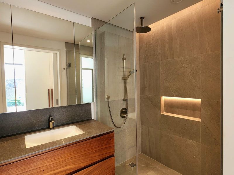 Modern bathroom featuring a floating wood vanity, integrated basin, large mirror cabinet, and a walk-in shower with stone tiling and recessed lighting.