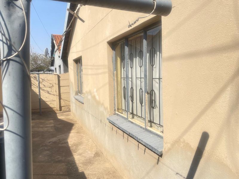 Rear exterior view of the property showing concrete paving, security bars on windows, and a precast concrete boundary wall.