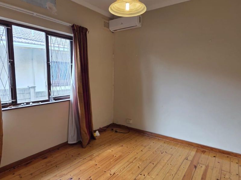 An empty bedroom featuring polished timber flooring, a wall-mounted air conditioning unit, and security bars on the window.