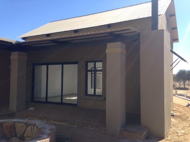 Rear exterior view of the property featuring a covered patio, sliding glass doors, and a stone fire pit in an unfinished garden area.