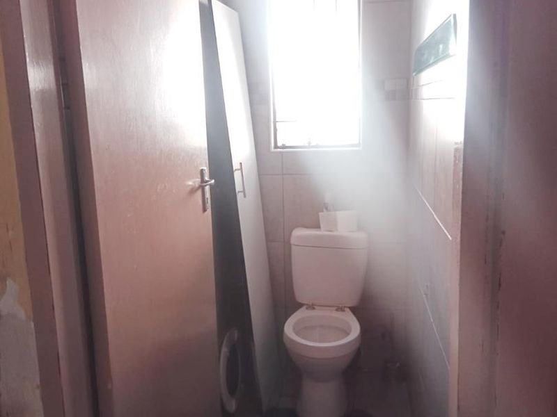 A compact bathroom featuring a standard toilet, tiled walls, and tiled flooring, requiring some cosmetic updates to improve its overall condition.