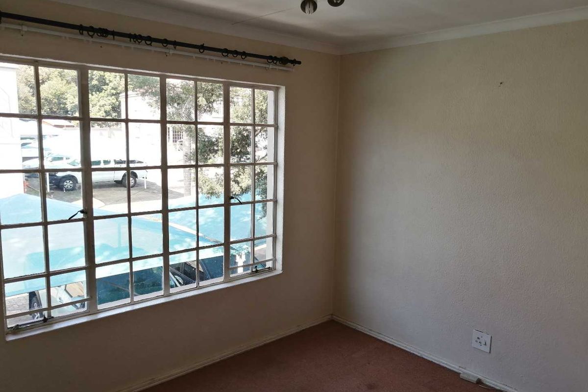 An empty bedroom featuring a large grid-pane window with security bars, neutral walls, and carpet flooring, offering a blank canvas for personalization.