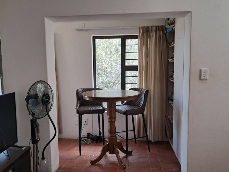 A living area featuring terracotta floor tiles, built-in shelving, and a window with security bars, showing signs of minor structural cracking.