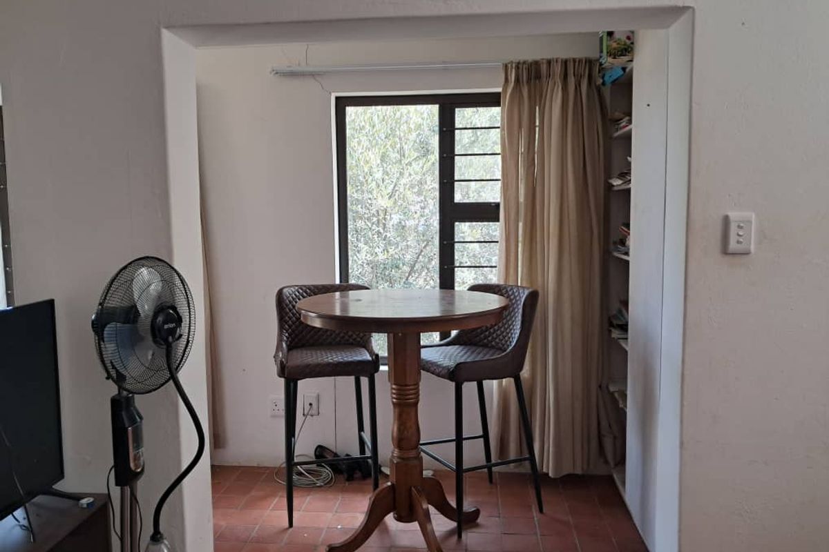 A living area featuring terracotta floor tiles, built-in shelving, and a window with security bars, showing signs of minor structural cracking.