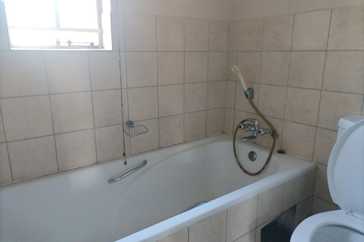 A functional bathroom featuring a built-in bathtub with a handheld shower attachment, tiled wall finishes, and a standard toilet.