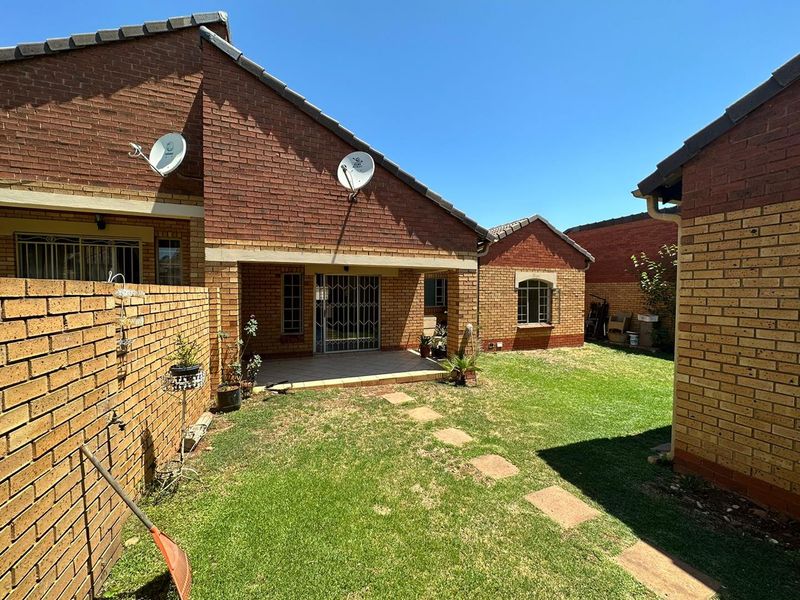 Rear view of the townhouse featuring a private garden, a covered patio area, and brick exterior walls.
