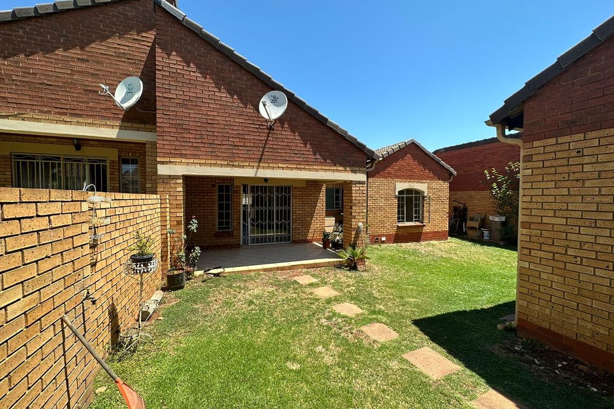 Rear view of the townhouse featuring a private garden, a covered patio area, and brick exterior walls.