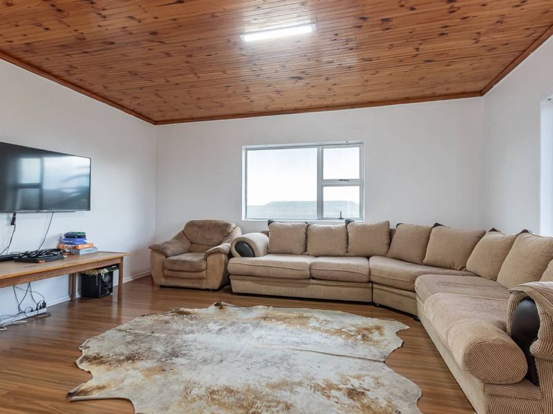 A living room featuring a timber tongue and groove ceiling, laminate flooring, and large windows providing natural light.