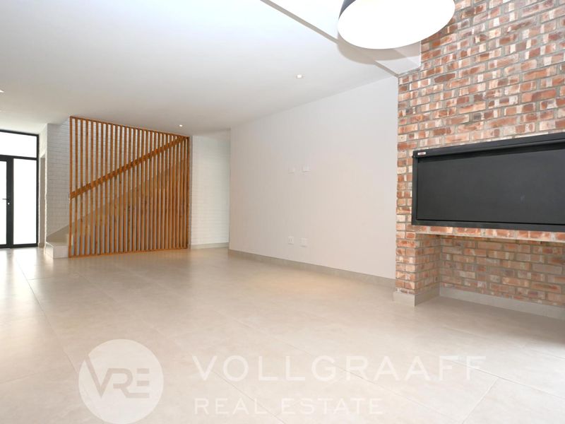 Spacious open-plan living area featuring a modern exposed brick fireplace, sleek tiled flooring, and a contemporary timber slat staircase partition.