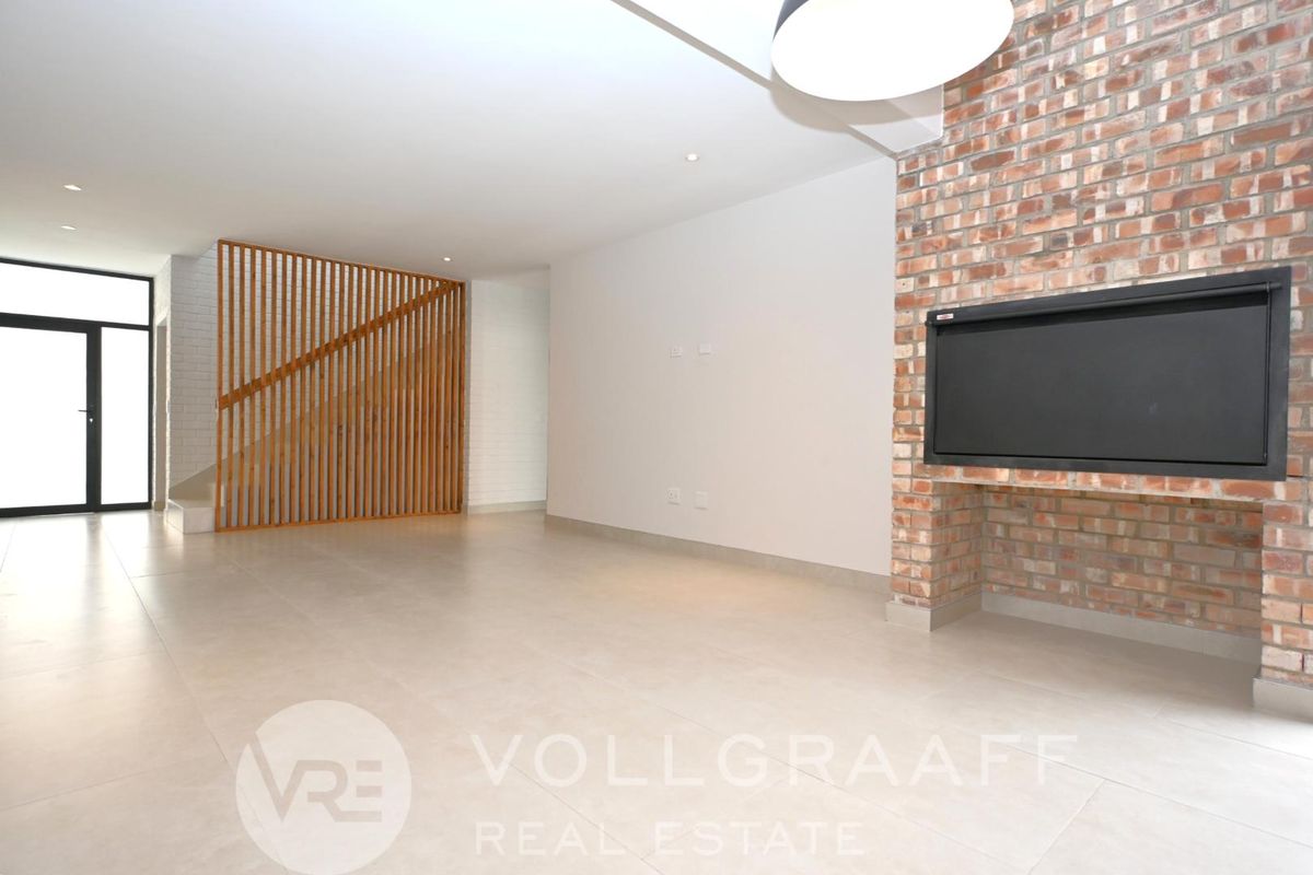 Spacious open-plan living area featuring a modern exposed brick fireplace, sleek tiled flooring, and a contemporary timber slat staircase partition.