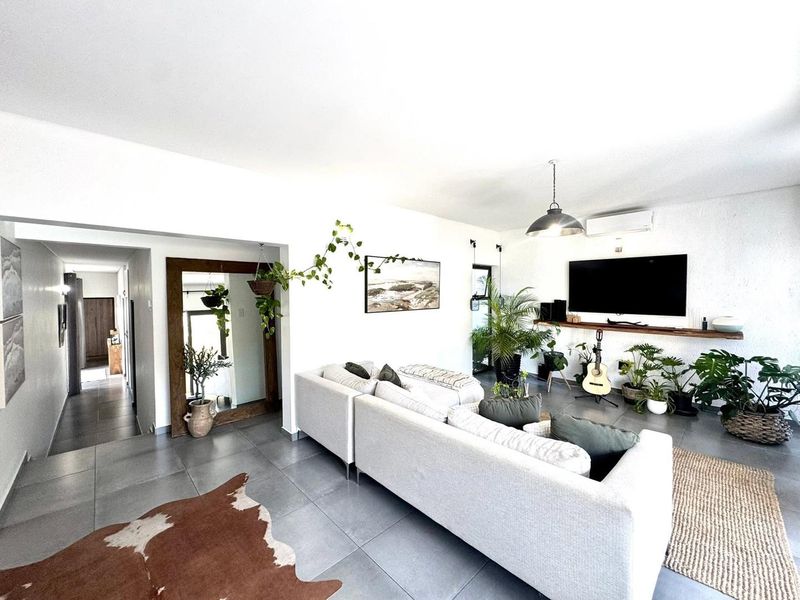 A bright and modern living room featuring large format floor tiles, a floating timber media shelf, and split-system air conditioning.
