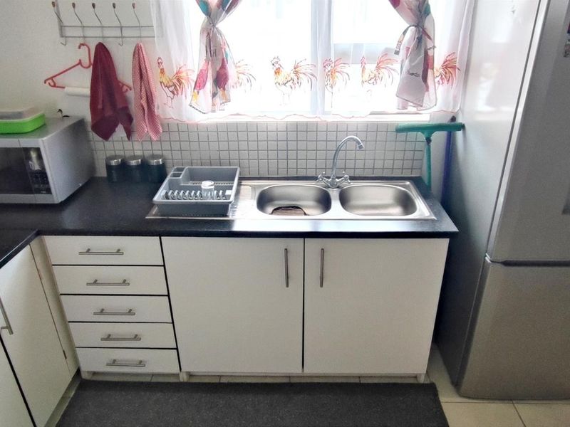 A functional kitchen area featuring a double bowl stainless steel sink, tiled splashback, laminate countertops, and white built-in cabinetry.
