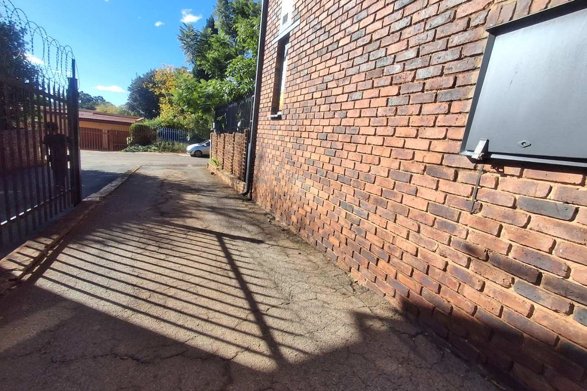 Exterior view of the property side path featuring exposed brick walling, security fencing, and paved driveway area.
