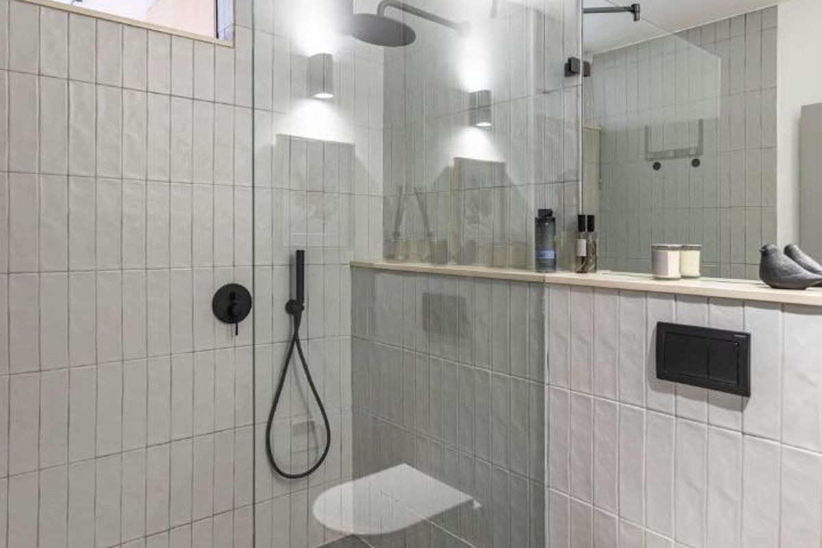 Modern bathroom featuring a walk-in shower with black matte fixtures, wall-mounted toilet, stone flooring, and large wall mirror with integrated shelving.