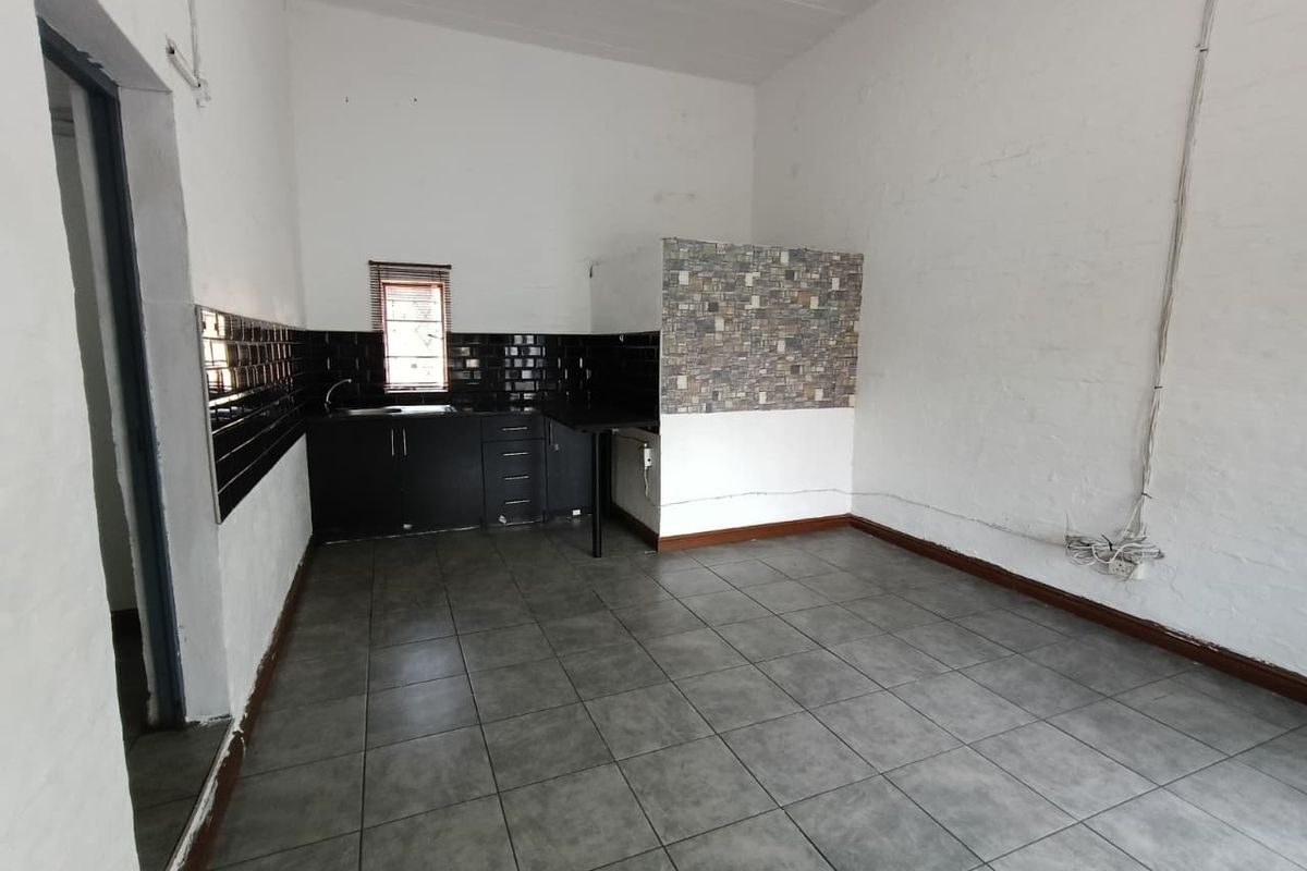 A compact, empty kitchen area featuring dark cabinetry, a tiled backsplash, and grey floor tiles, suitable for a small industrial or office workspace.