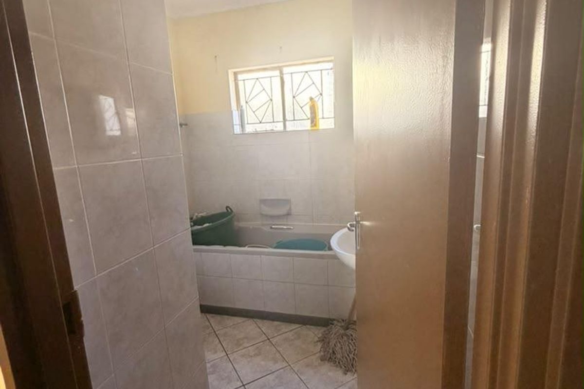 A functional bathroom featuring tiled walls and flooring, a built-in bathtub, and a pedestal basin, requiring some cosmetic updates.