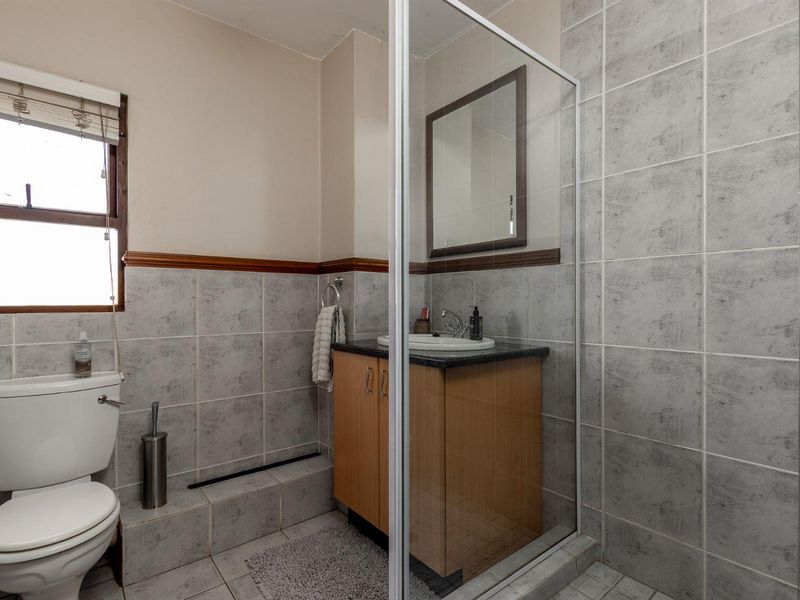 A functional bathroom featuring a shower enclosure, vanity cabinet with basin, and toilet, finished with neutral wall and floor tiling.