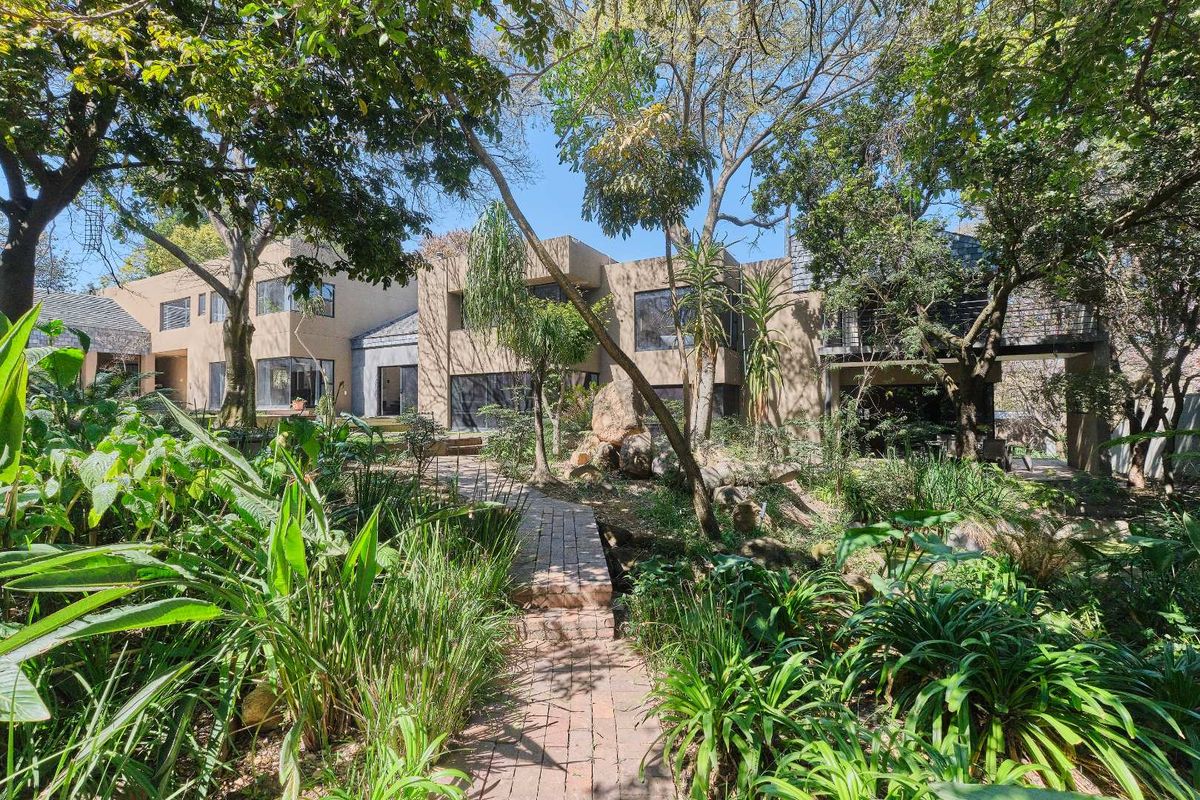 A view of the rear building facade featuring a brick pathway leading through a lush, mature garden with established trees and a balcony.