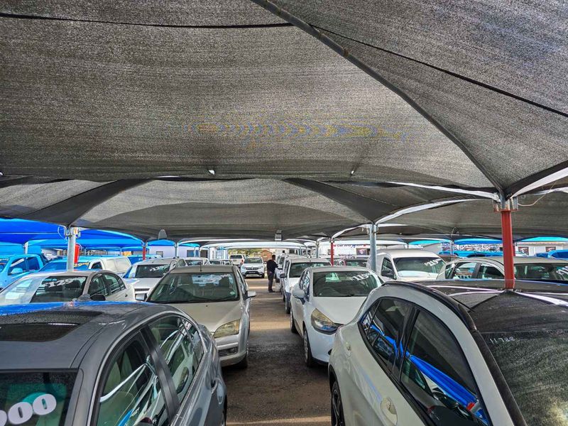 An outdoor vehicle display area featuring a large overhead shade cloth canopy supported by steel poles.