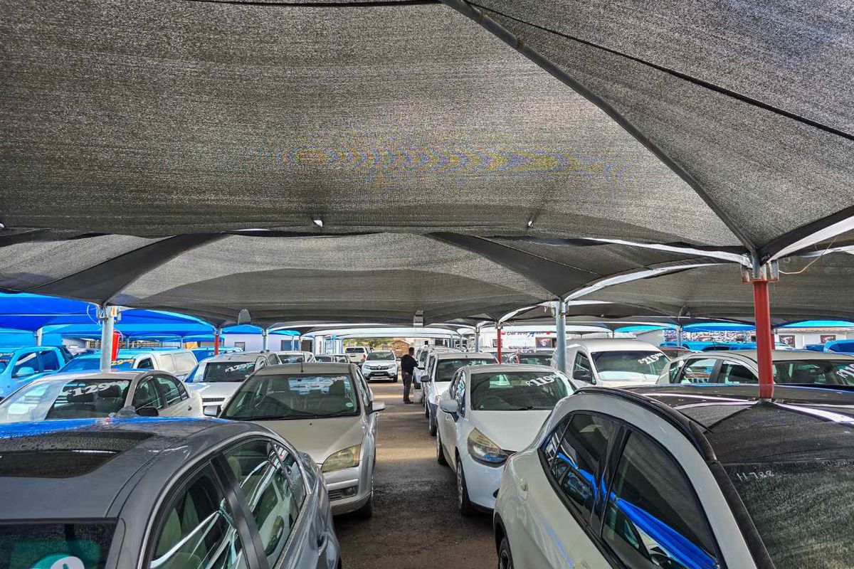 An outdoor vehicle display area featuring a large overhead shade cloth canopy supported by steel poles.