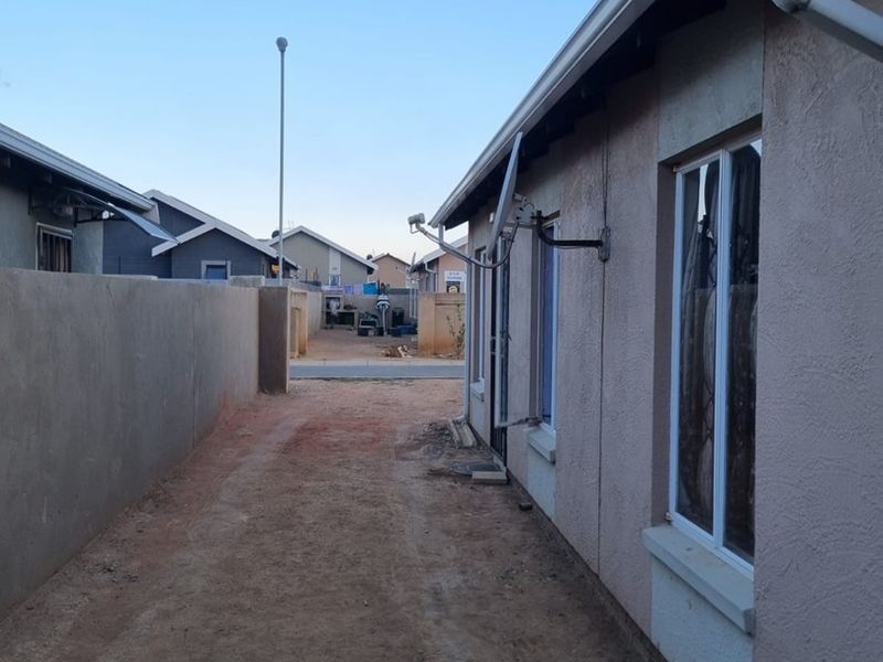 A side exterior view of the property showing a narrow unpaved pathway, boundary wall, and installed exterior utility fixtures.