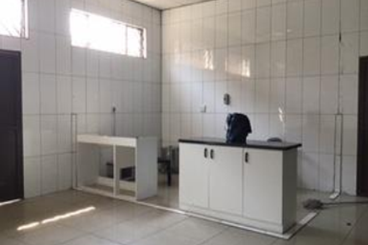 A sparse, tiled kitchen area featuring basic built-in cabinetry and fluorescent lighting, requiring cosmetic updates to improve functionality and aesthetic appeal.
