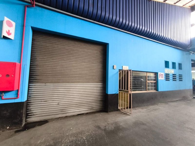 Industrial unit exterior featuring a large roller shutter door, security gate, and fire safety equipment, with a durable concrete floor and blue painted facade.