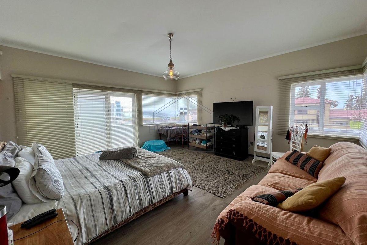 Spacious bedroom featuring wood-look flooring, large windows with fitted blinds, and a central pendant light fixture.