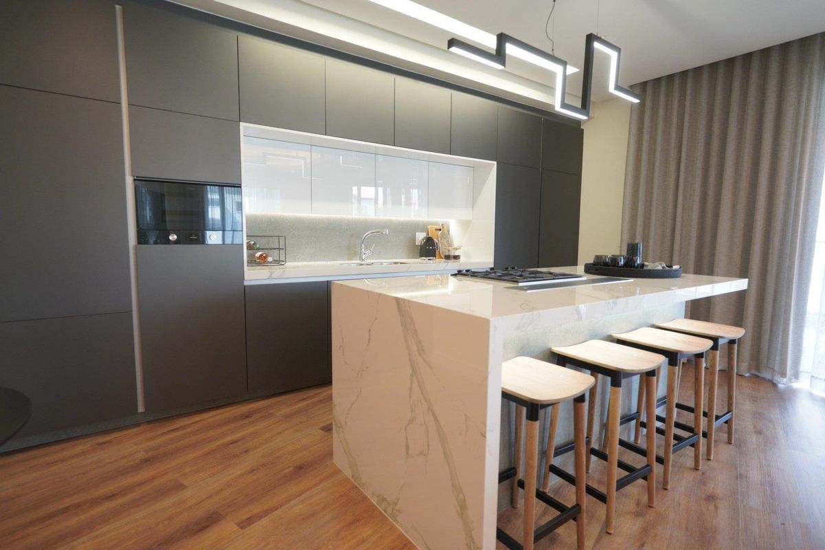 Modern kitchen featuring sleek dark cabinetry, a marble-look stone island with integrated cooktop, and contemporary pendant lighting in an open-plan layout.