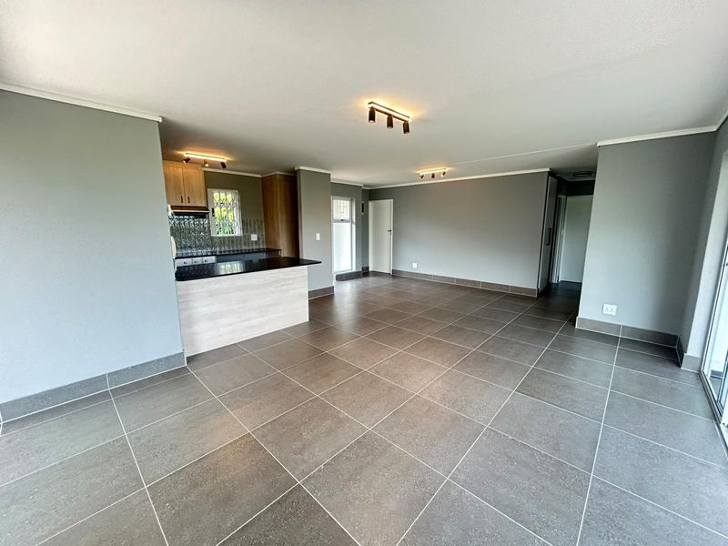 Spacious open-plan living area featuring modern grey floor tiles, neutral wall tones, and a functional kitchen with granite countertops and a breakfast bar.