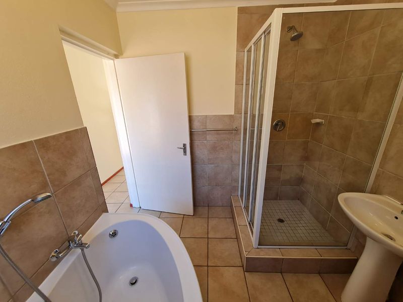 A functional bathroom featuring a separate shower enclosure, pedestal basin, and bathtub with neutral wall and floor tiling.