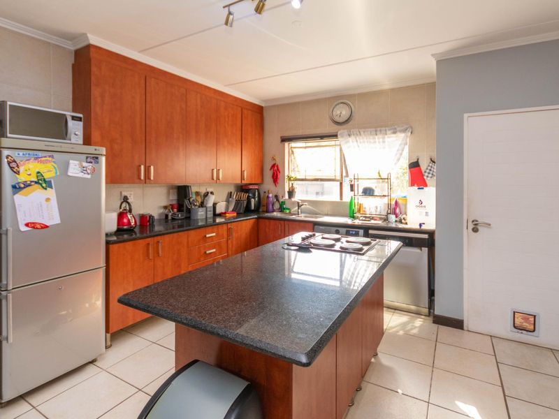 Functional kitchen featuring wood-finish cabinetry, granite countertops, a central island with a built-in hob, and tiled flooring.
