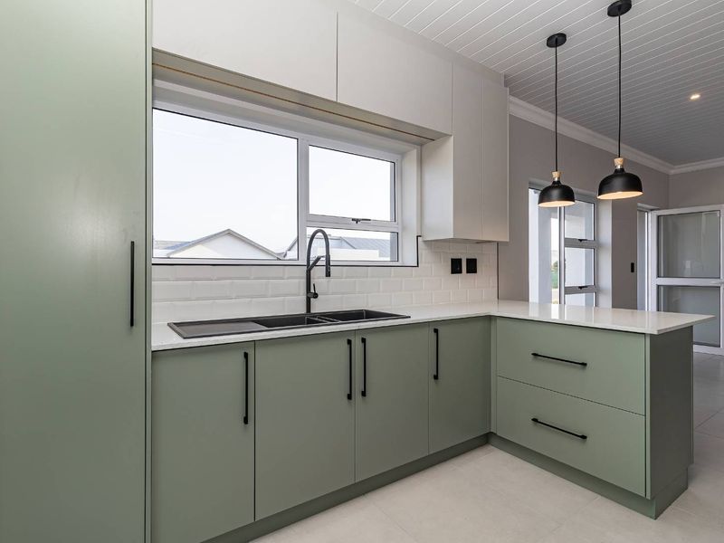 Modern kitchen featuring sage green cabinetry, white quartz countertops, subway tile backsplash, and contemporary black fixtures in a bright, clean space.