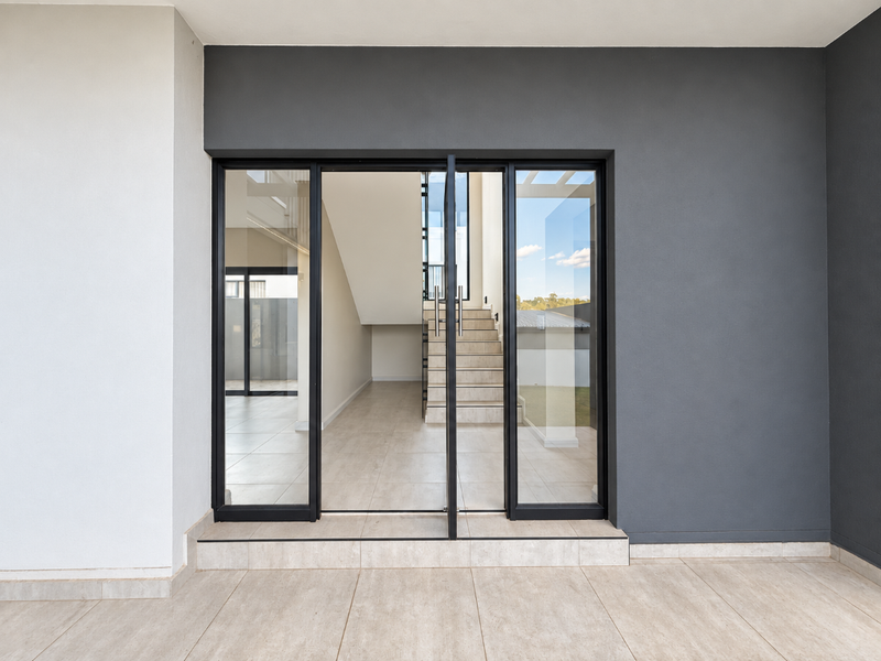 Modern entrance featuring a large glass pivot door, tiled flooring, and a clear view into the bright, open-plan interior with a staircase.