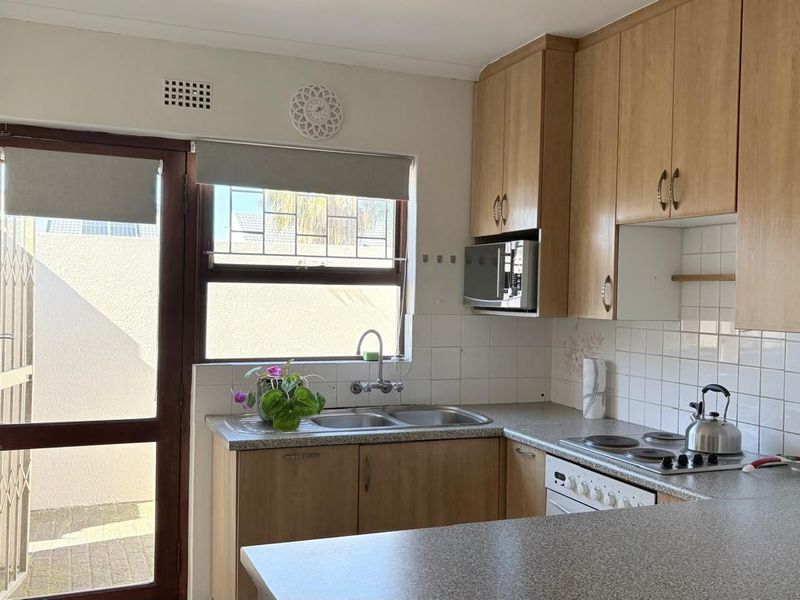 Functional kitchen featuring light wood-finish cabinetry, laminate countertops, a double sink, and an integrated electric hob with a tiled backsplash.