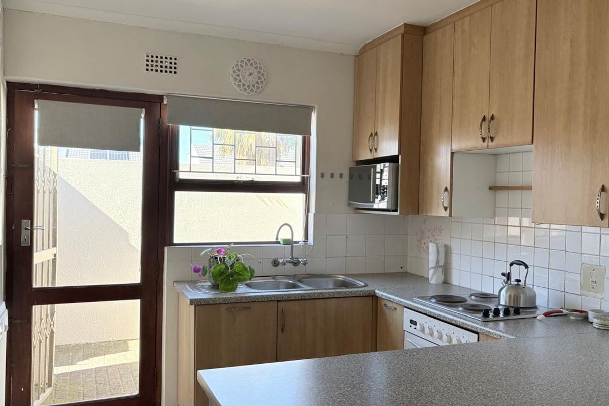 Functional kitchen featuring light wood-finish cabinetry, laminate countertops, a double sink, and an integrated electric hob with a tiled backsplash.