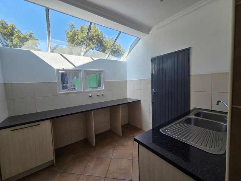 A bright and functional scullery featuring a double sink, granite countertops, tiled splashbacks, and a large skylight providing ample natural light.
