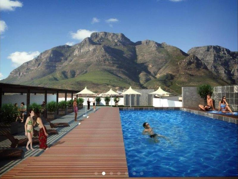 A rooftop swimming pool area featuring timber decking, a stone feature wall, and a pergola, set against a scenic mountain backdrop.