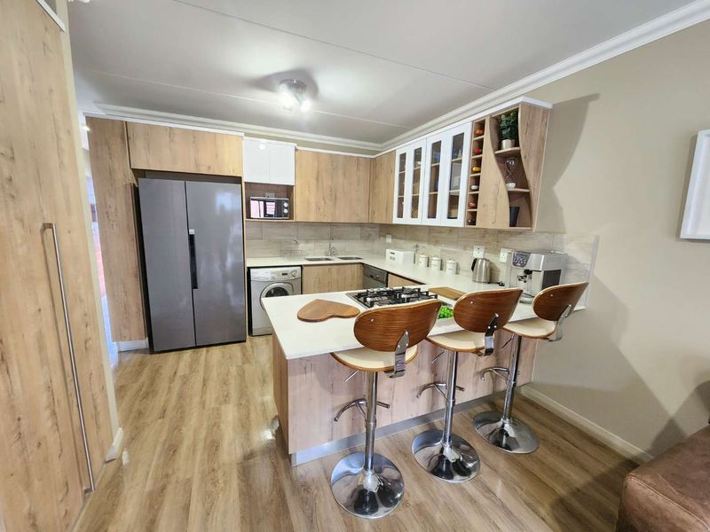 Modern kitchen featuring wood-look cabinetry, a gas hob, breakfast bar, and integrated appliances, finished with light-toned laminate flooring and a tiled backsplash.