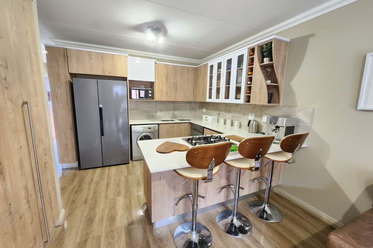 Modern kitchen featuring wood-look cabinetry, a gas hob, breakfast bar, and integrated appliances, finished with light-toned laminate flooring and a tiled backsplash.