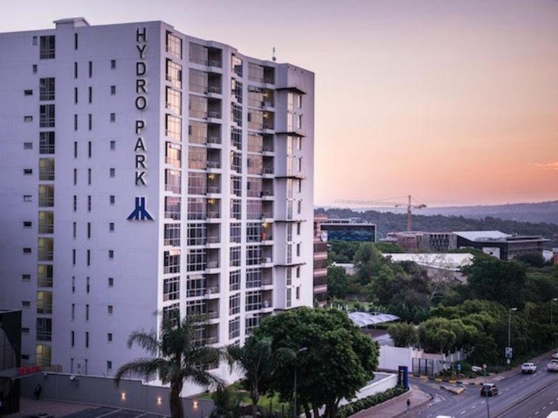 A high-rise apartment building exterior featuring modern architecture, balconies, and large windows, set against a scenic sunset backdrop.