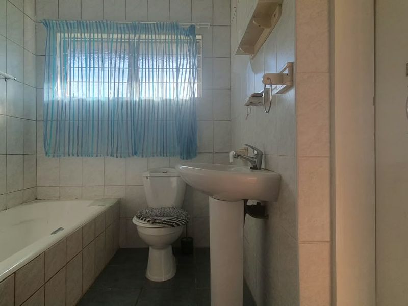 A functional bathroom featuring a pedestal washbasin, built-in bathtub, and toilet, finished with tiled walls and flooring.