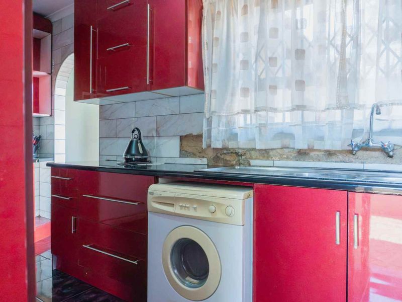 Kitchen featuring glossy red cabinetry, black granite countertops, and a tiled backsplash with visible areas requiring repair and finishing.