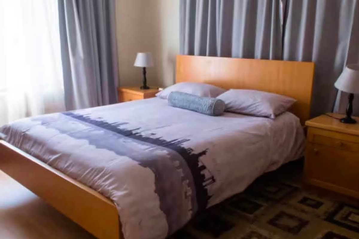 A functional bedroom featuring laminate flooring and neutral window treatments, providing a comfortable and well-lit sleeping space.