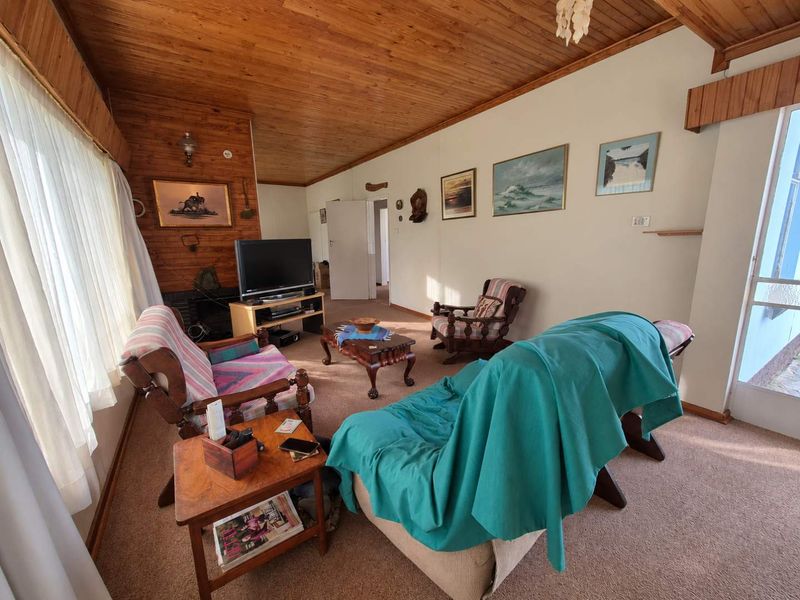 A living room featuring a timber-clad ceiling and feature wall, a fireplace, and carpeted flooring, offering a warm and traditional aesthetic.