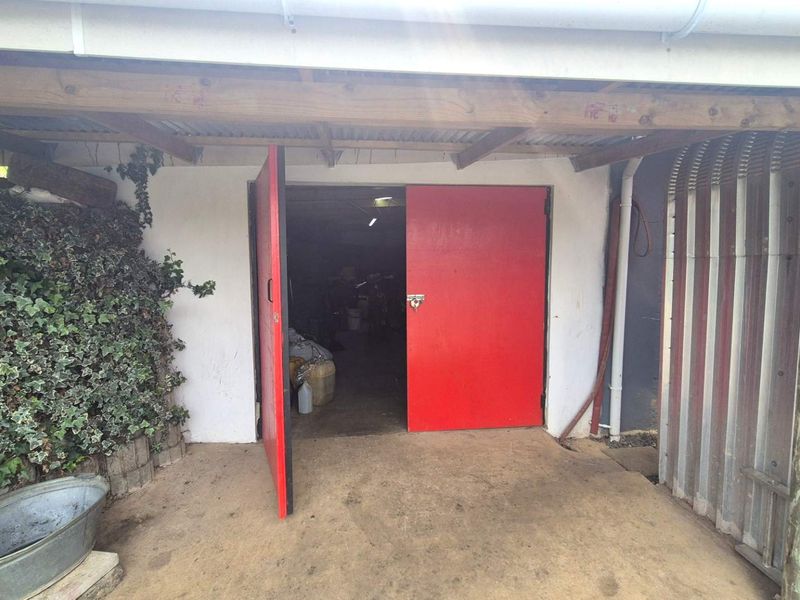A functional garage space featuring double red steel doors, exposed timber rafters, and a corrugated iron roof structure.