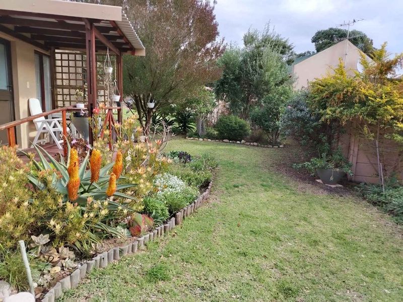 A well-maintained rear garden featuring a timber deck with a pergola, established landscaping, and a lawn area.